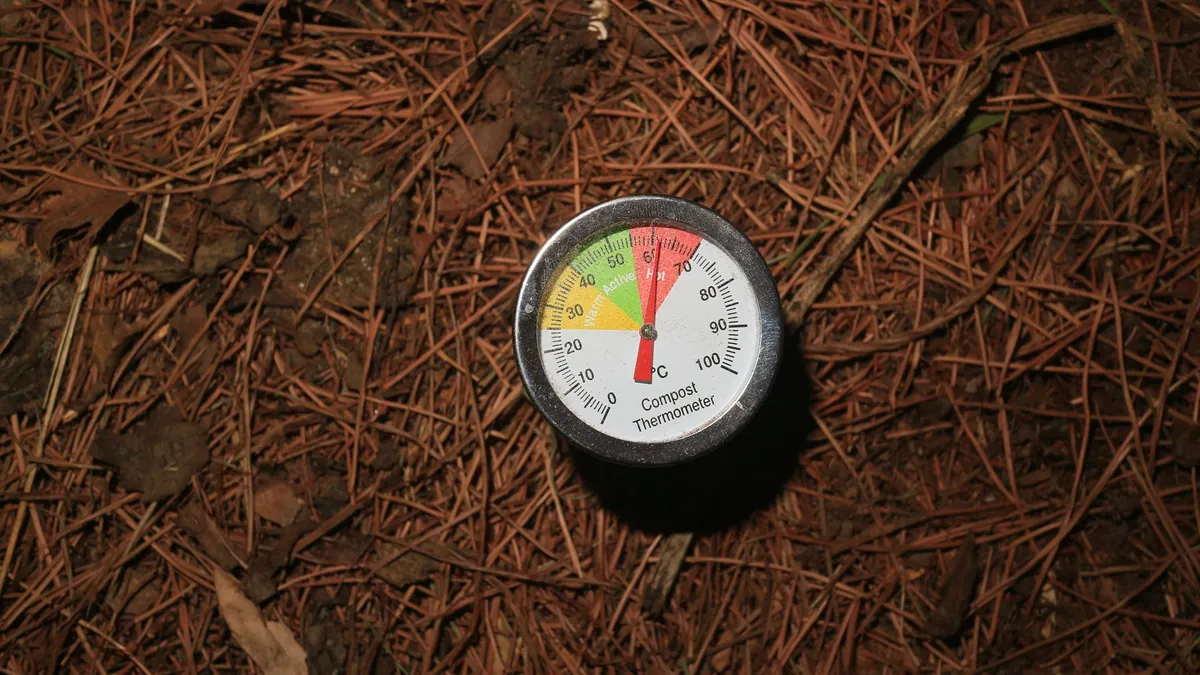 Long-stemmed compost thermometer pushed into dark compost to read the internal temperature of the pile