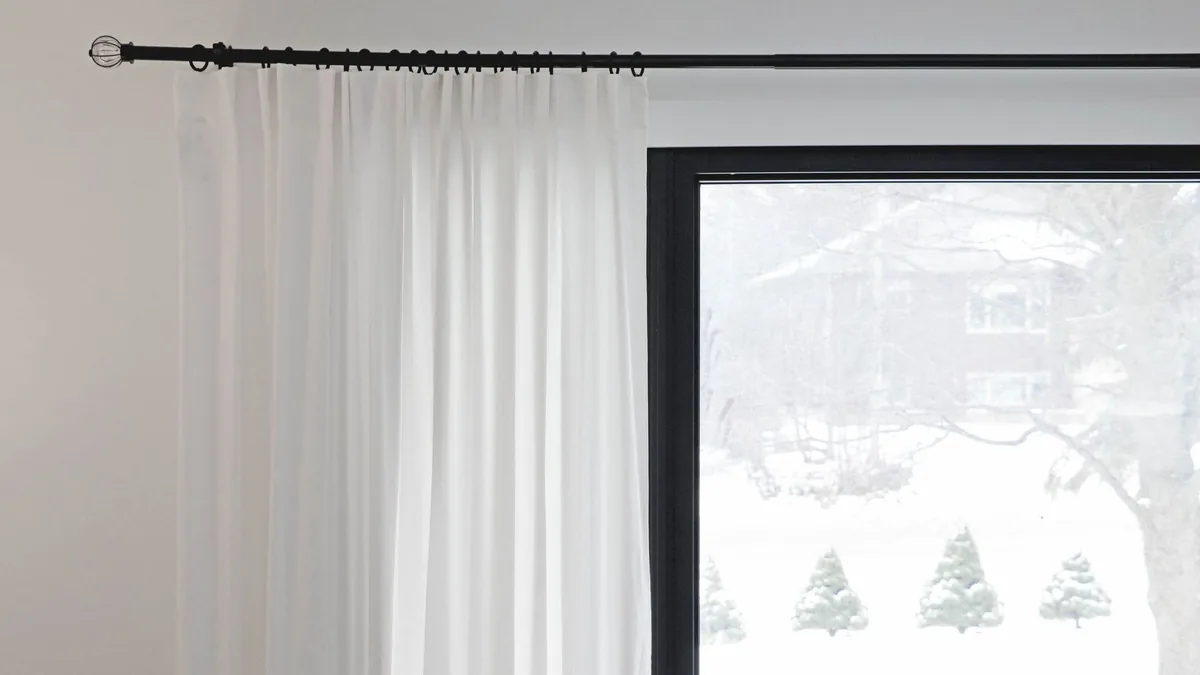 White curtains partially covering a window with a snowy view outside