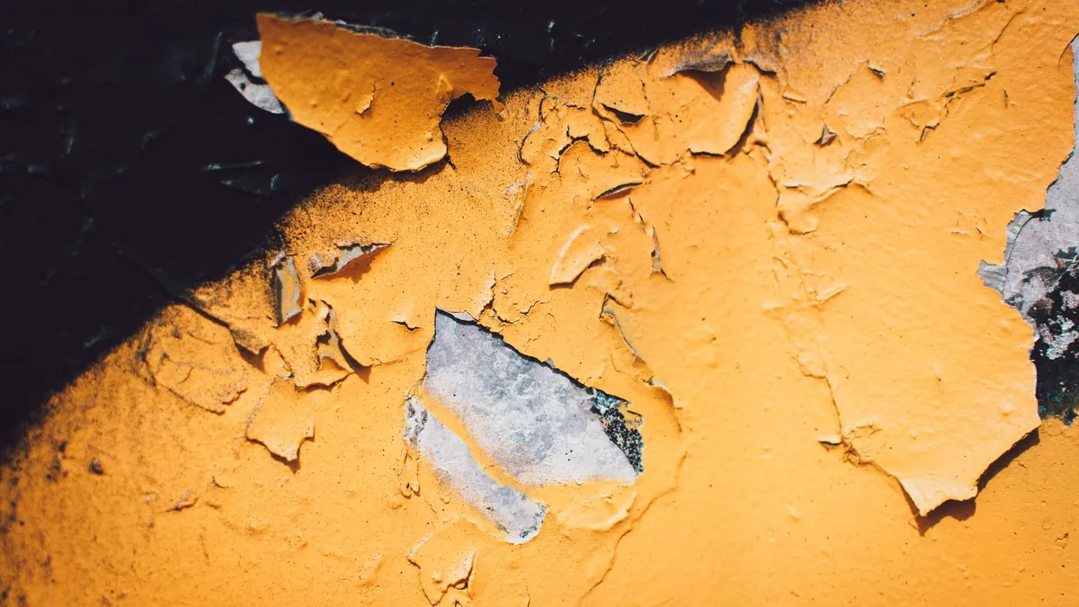 Close-up of a painted wall with peeling paint showing bare patches where the coating lost its grip